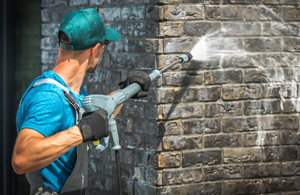 A man pressure washing the brick wall of the house.